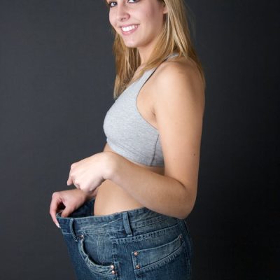 Happy woman in oversized jeans, celebrating weight loss in a studio setting.