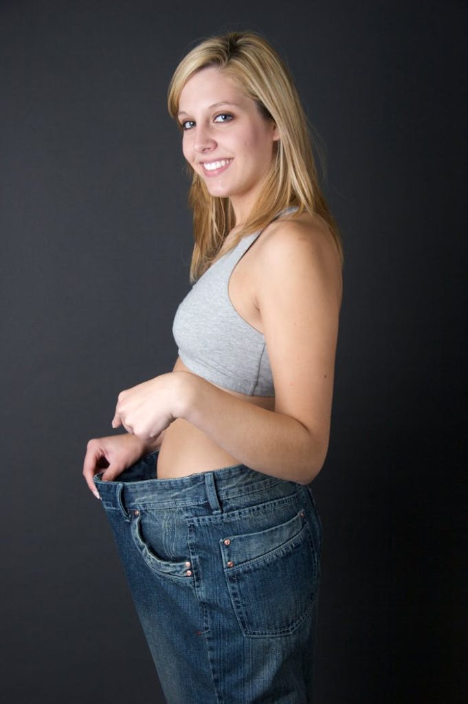 Happy woman in oversized jeans, celebrating weight loss in a studio setting.