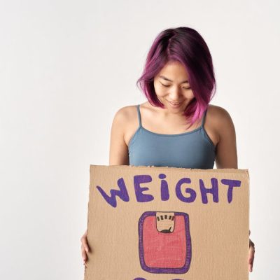 Asian woman holding a cardboard sign about weight loss in a studio setting.