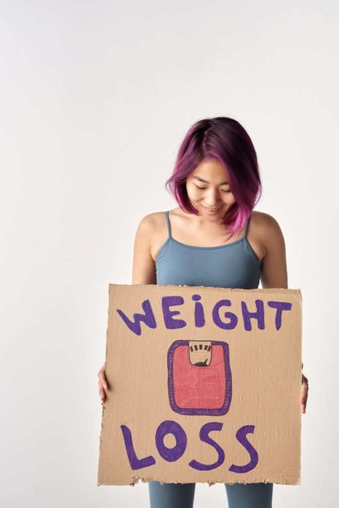 Asian woman holding a cardboard sign about weight loss in a studio setting.