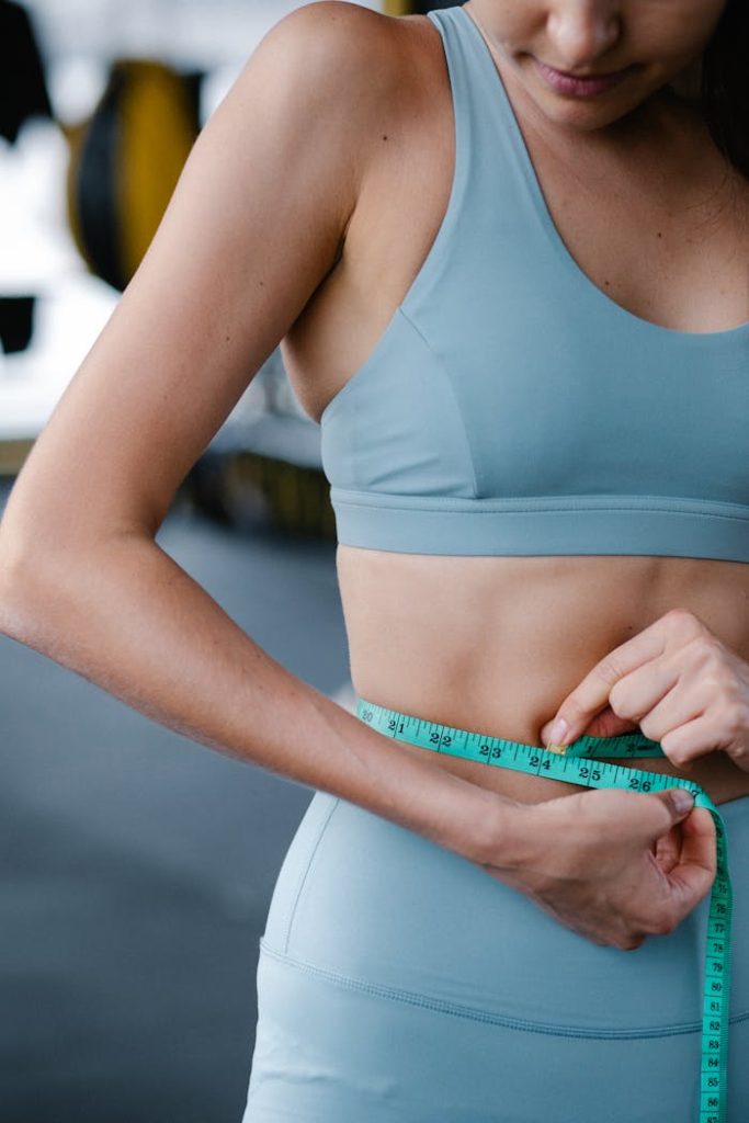Female athlete measuring waistline with tape for health tracking in gym.