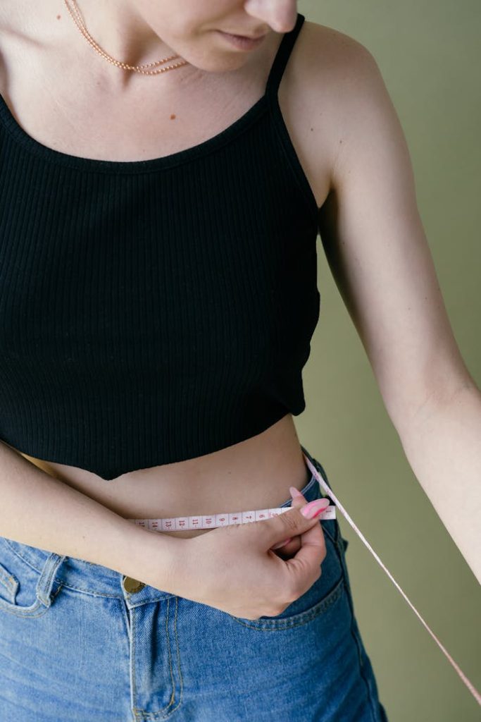 Close-up of a woman measuring her waist with a tape, focusing on health and fitness goals.